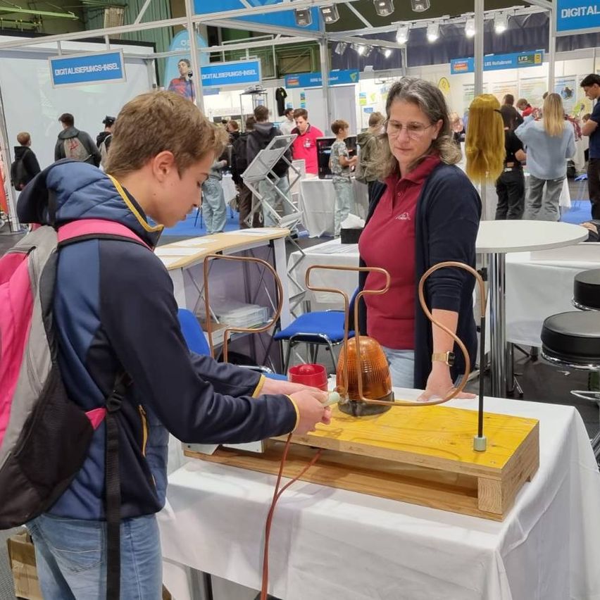 Ein junger Mann demonstriert ein wissenschaftliches Experiment mit einer Kupferspule und einer Batterie auf einer Wissenschaftsmesse.