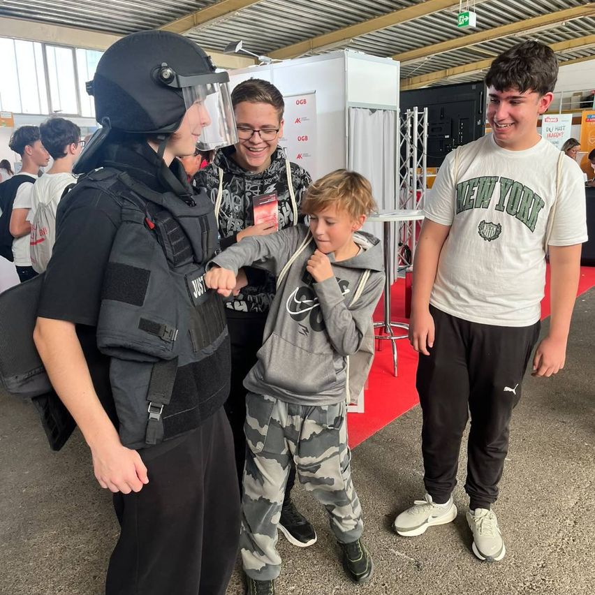 Eine Person in einer Aufständischenpolizei-Uniform steht neben einem jungen Jungen in einer Tarnjacke, während eine Frau mit Brille und ein Mann in einem New York-Shirt in der Nähe stehen.