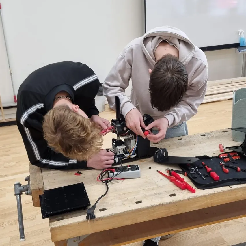 Zwei Jugendliche bei der Arbeit an einem elektronischen Gerät in einem Werkraum.