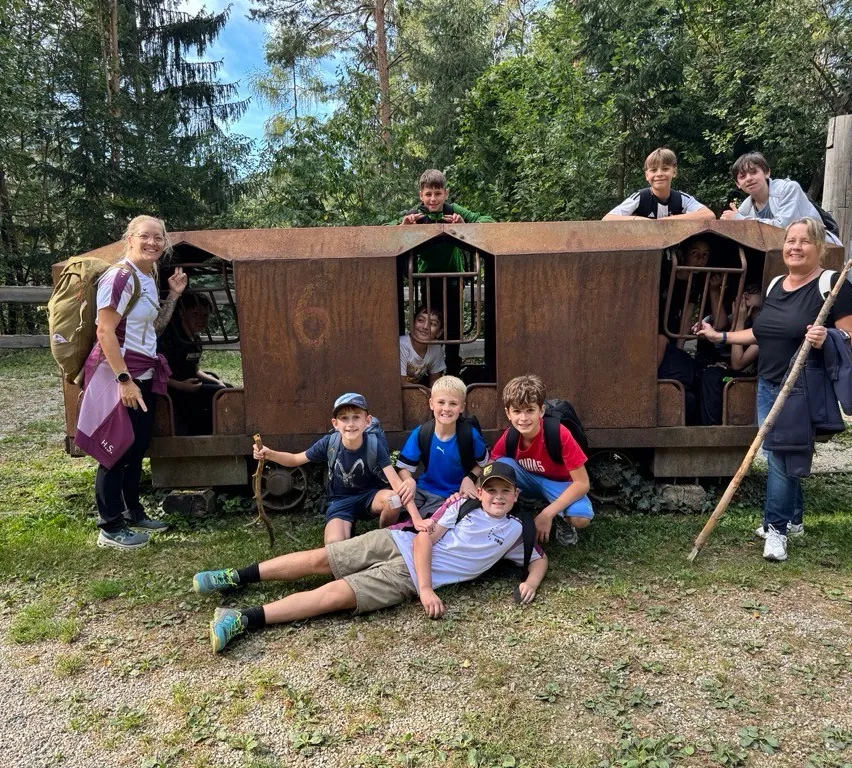 Eine Gruppe von Kindern und Erwachsenen posiert für ein Foto vor einem rostigen Waggon.