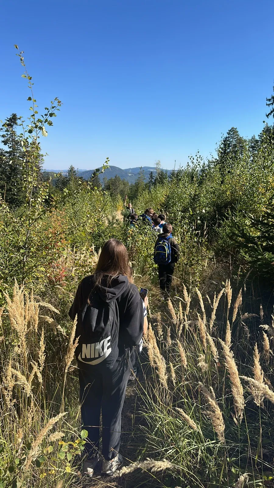Eine Gruppe von Menschen wandert durch einen dichten Wald. Eine Person trägt einen Nike-Rucksack.