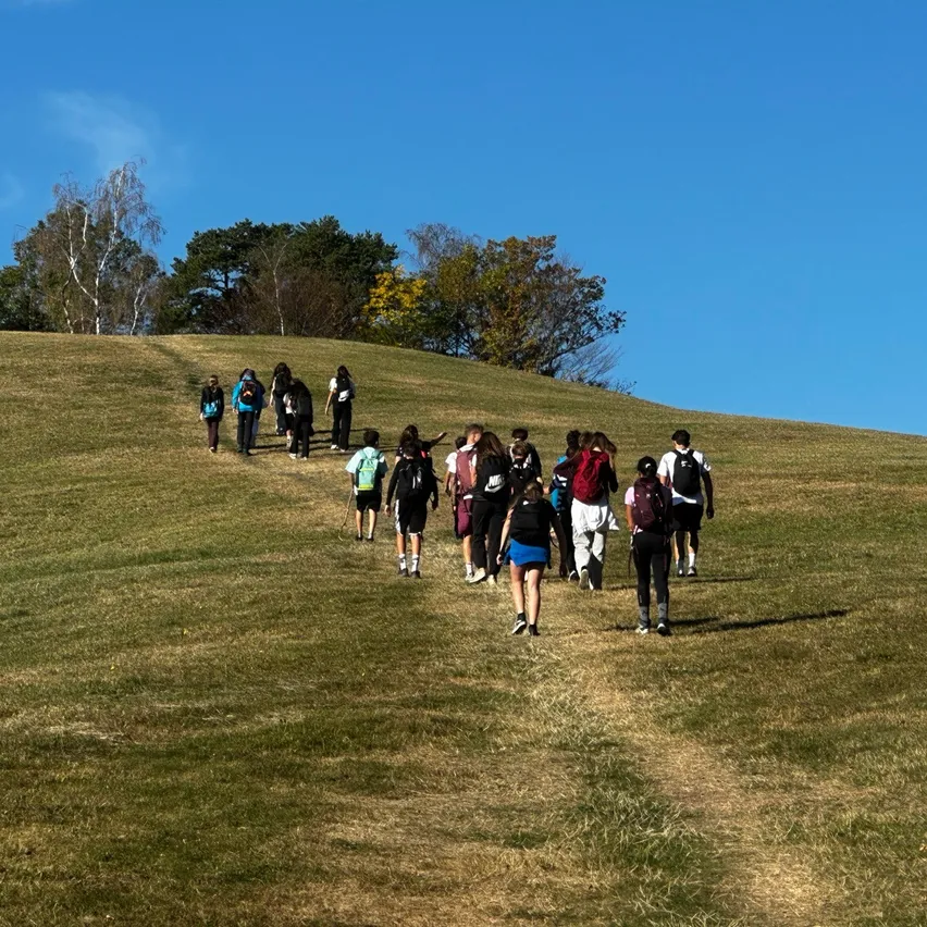 Eine Gruppe von Schülern geht an einem sonnigen Tag einen Grashügel hinauf.
