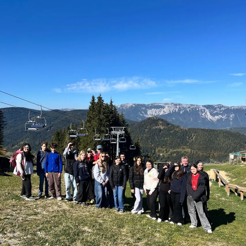 Eine Gruppe von Menschen steht auf einem Grasfeld mit einem Bergrücken im Hintergrund.