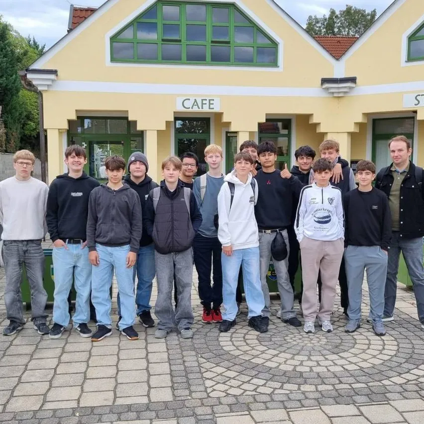 Eine Gruppe junger Männer und Jungen posiert für ein Foto vor einem gelben Gebäude mit dem Schild 'Steinfeld - Zentrum'.