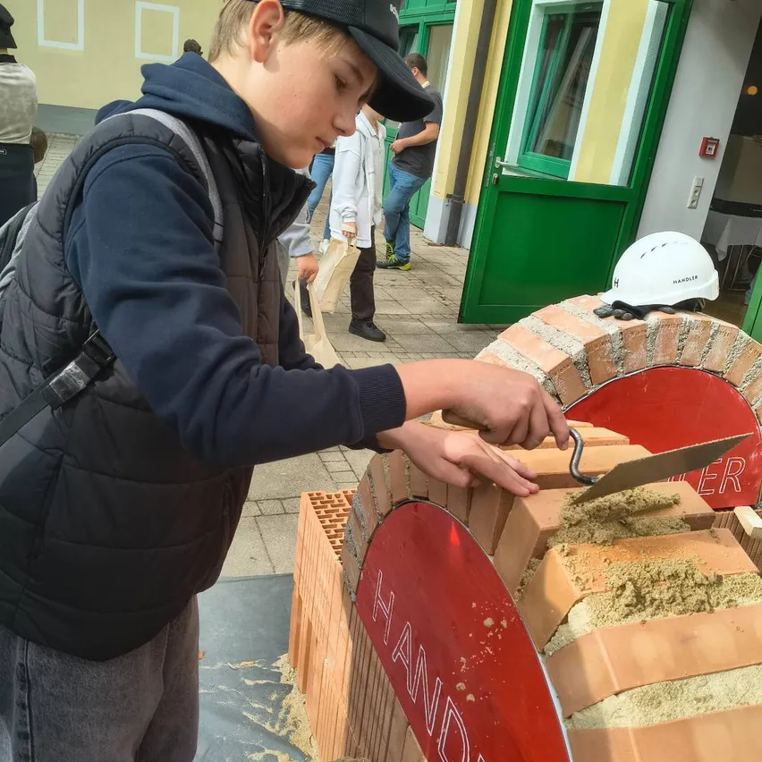 Ein junger Junge, der eine schwarze Kappe und einen schwarzen Mantel trägt, arbeitet mit einem Meißel an einem Backofen.