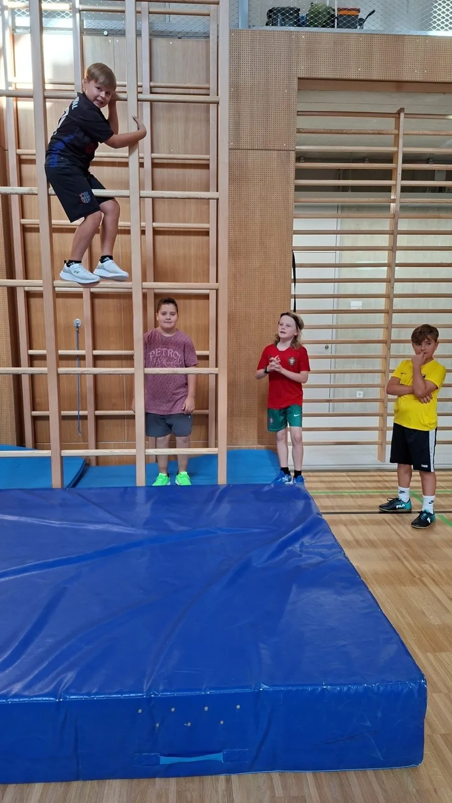 Ein Junge klettert in einem Fitnessstudio auf eine Holzleiter, während drei andere Kinder zusehen.