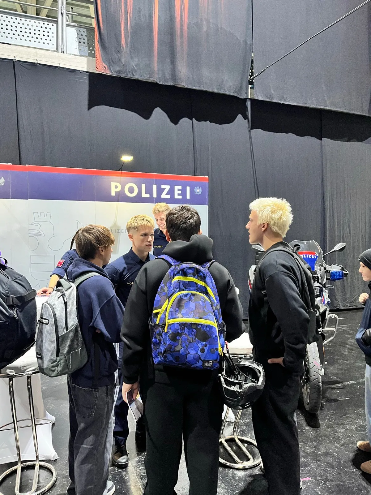 Eine Gruppe junger Männer in Uniformen versammelt sich um ein Schild, das 'POLIZEI' steht. Sie schauen auf etwas auf dem Boden.