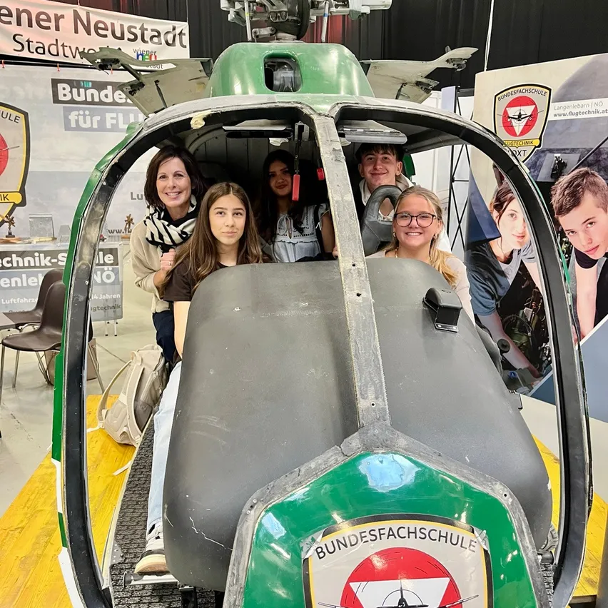 Fünf Personen sitzen in einem Helikoptersimulator und lächeln für ein Foto.