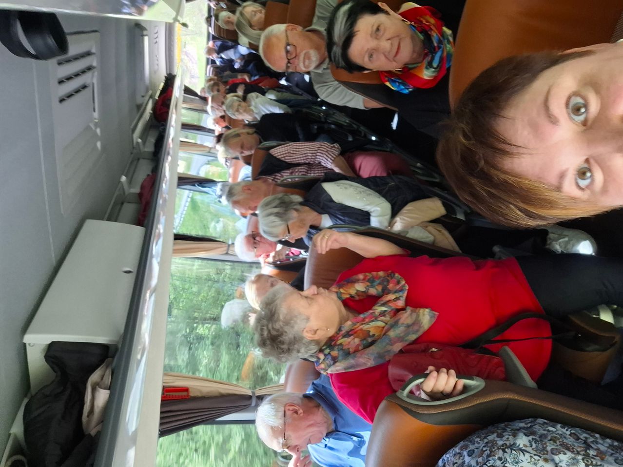 Ein Bus ist mit älteren Menschen an einem sonnigen Tag gefüllt, die mit verschiedenen Gesichtsausdrücken sitzen, einige mit Brille.