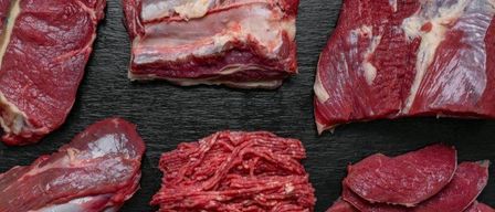 Verschiedene rohe Rindfleischstücke sind auf einer schwarzen Oberfläche zu sehen, darunter Steaks, Hackfleisch und Rippen.