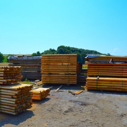 Ein Stapel gebundener Holzstämme, bereit für den Transport in einer ländlichen Umgebung mit einem klaren blauen Himmel im Hintergrund.