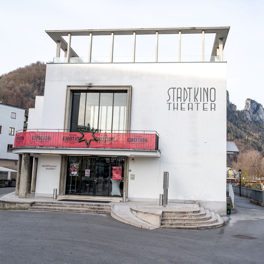 Das moderne weiße Gebäude des Stadtkino Theaters befindet sich vor einem Berg, mit einer Terrasse und Glastüren, die zum Eingang führen.