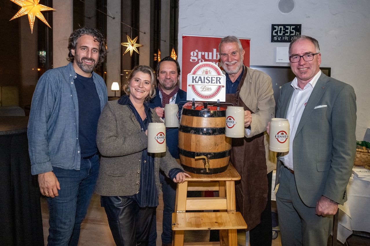 Fünf Personen stehen hinter einem Fass mit der Aufschrift 'Kaiser Bier'. Der Mann rechts trägt eine Brille, die anderen halten Tassen. Eine digitale Uhr zeigt 20:35 an.