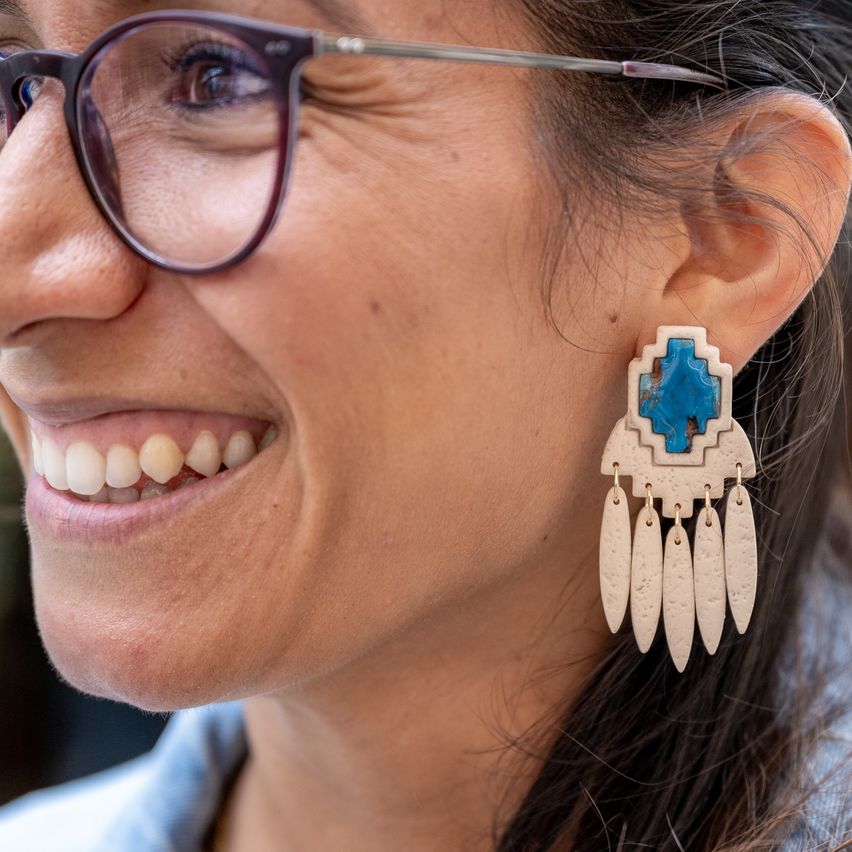 Eine Frau mit Brille lächelt und zeigt ein Nahaufnahme ihres Gesichts mit türkisen und weißen Ohrringen.