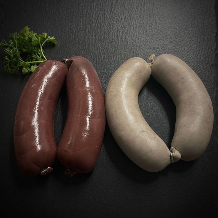 Drei Würste, darunter zwei braune und einer weißer, sind auf einer schwarzen Oberfläche zu sehen. Ein Petersilienzweig befindet sich links von den Würsten.