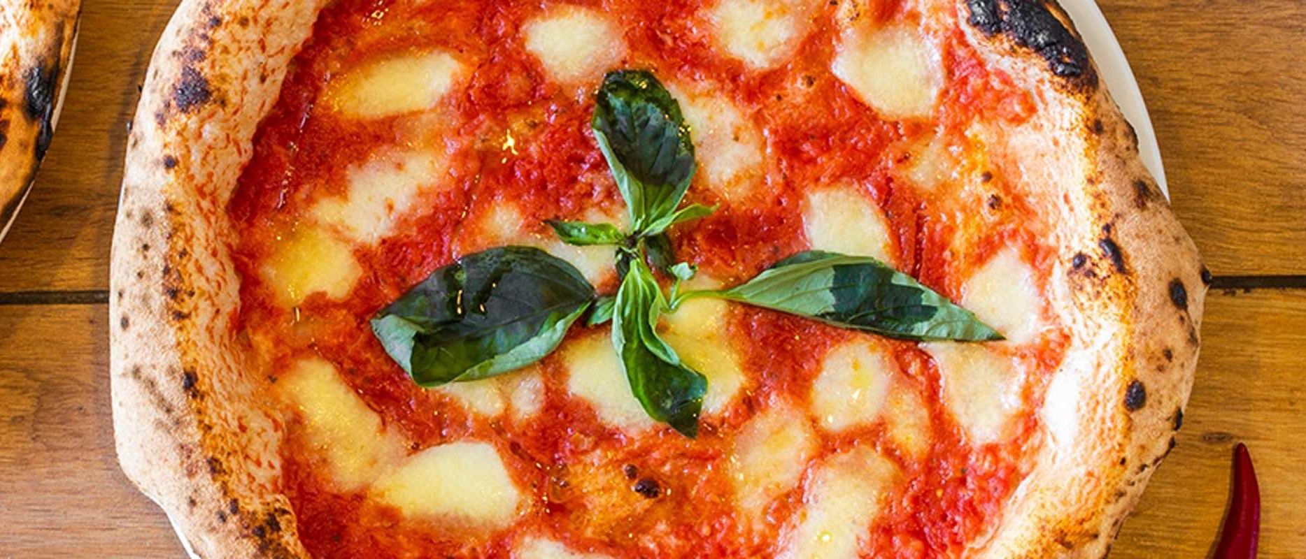 Ein Nahaufnahme einer Pizza mit roter Soße, geschmolzenem Käse und Basilikumblättern obenauf.