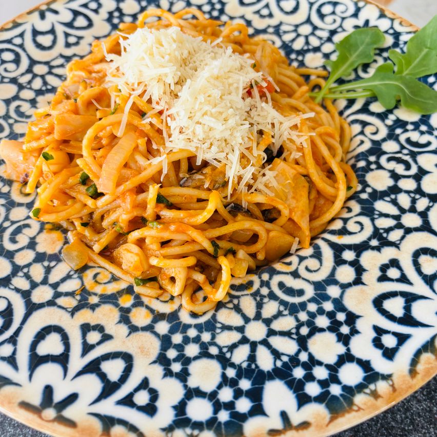 Ein Teller mit Nudeln und Tomatensauce, überbacken mit Käse. Dazu eine Beilage aus Rucola.