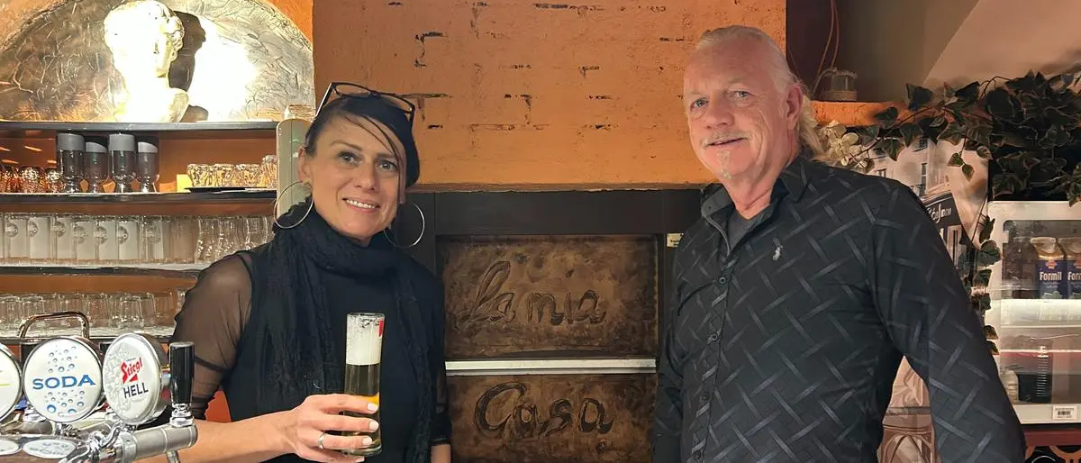 Ein Mann und eine Frau lächeln vor einer Wand mit den Worten Lama Casa in die Kamera.