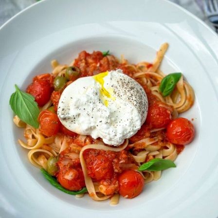 Ein Teller mit Pappardelle-Pasta mit Kirschtomaten, einem pochierten Ei und Basilikumblättern obenauf.