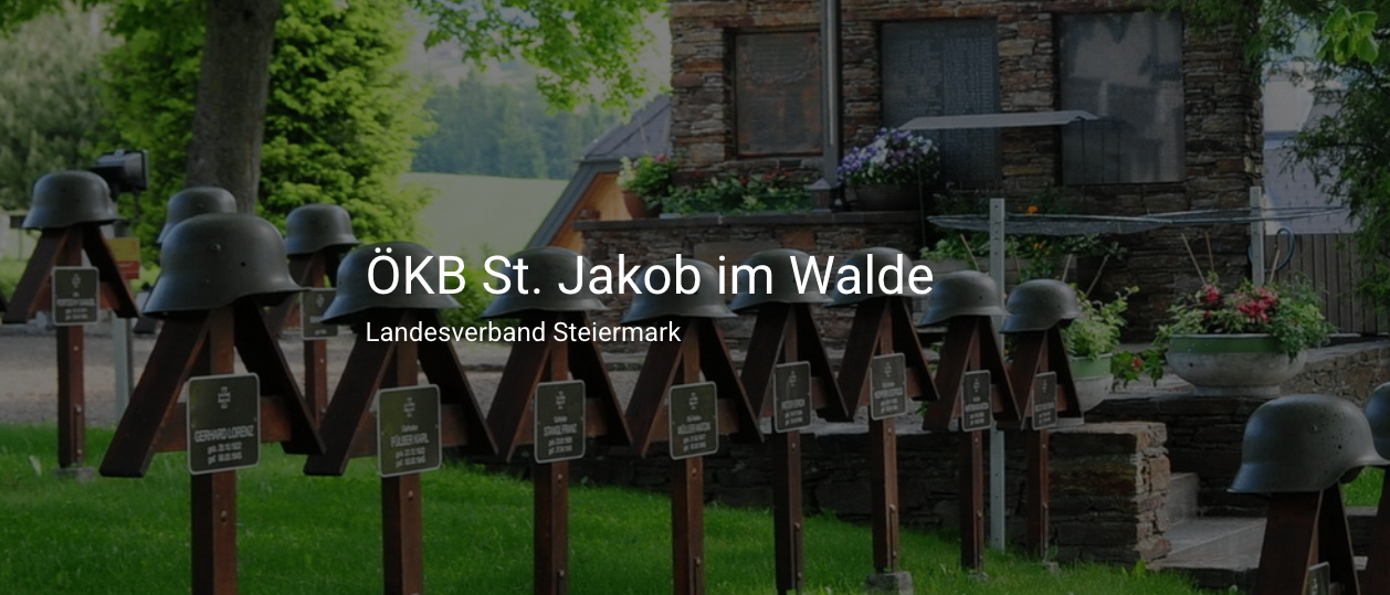 Eingangsbereich mit Helmen und Plaketten neben einem Gebäude mit Garten. Das Gebäude trägt die Aufschrift ÖKB St. Jakob im Walde, Landesverband Steiermark.