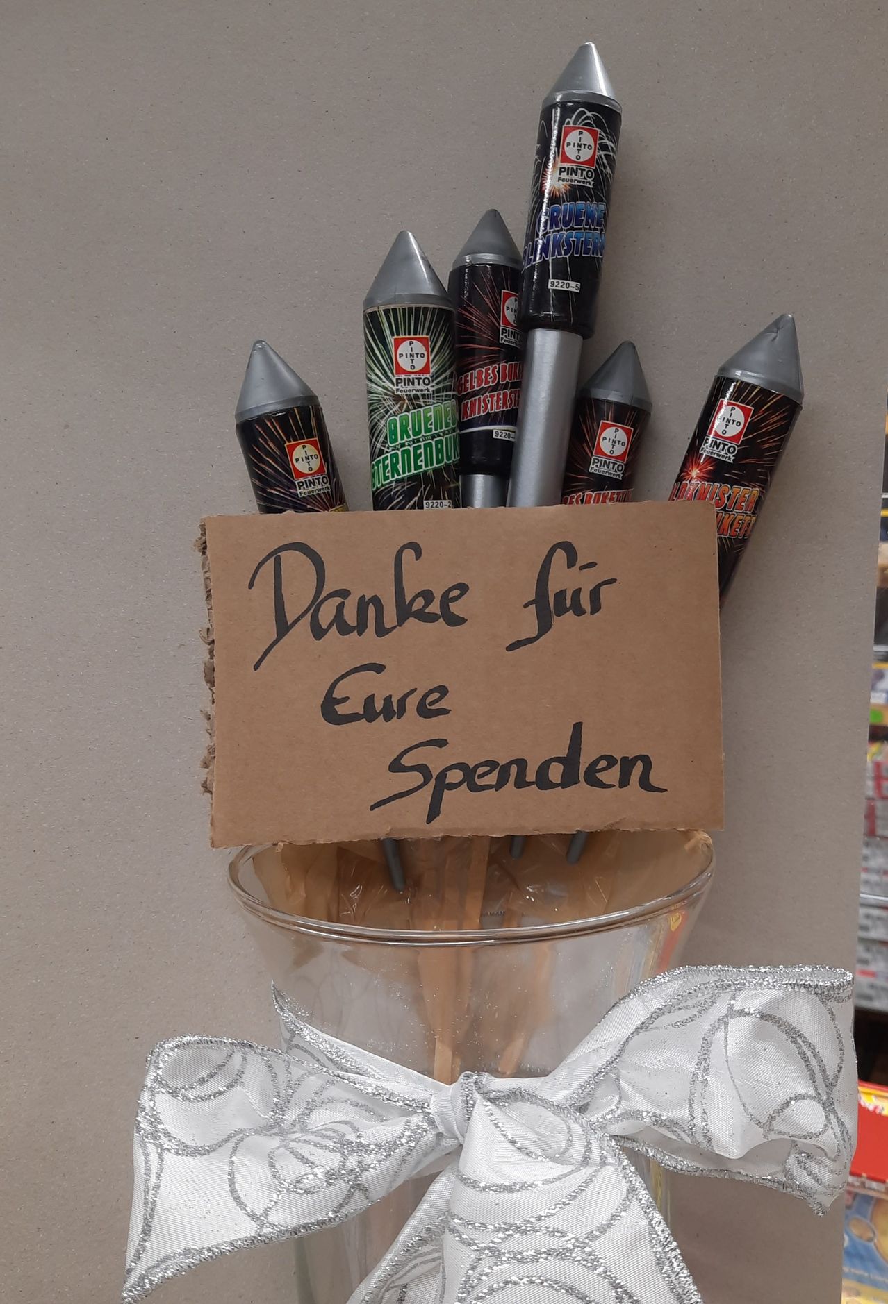 Ein Pappschild mit der Aufschrift Danke fur Eure Spenden steht über einer Sammlung von Feuerwerkskörpern in einer Glasschale.