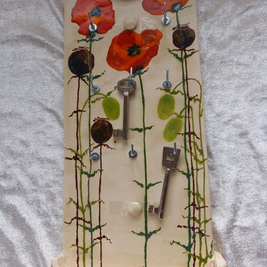 Ein dekorativer Schlüsselhaken mit Blumenthema, mit gemalten roten Mohnblumen und grünen Blättern. Drei Schlüssel sind rechts am Haken befestigt.