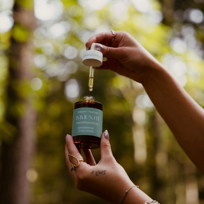 Eine Person hält eine Flasche Immun Fit in der Hand und tropft ein paar Tropfen in ihre Handfläche. Die Flasche hat ein grünes Etikett mit weißen Schriftzeichen.