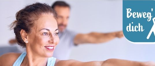 Eine Frau und ein Mann machen Yoga in einem Raum. Die Frau lächelt und streckt ihre Arme. Der Mann steht hinter ihr. Die Worte 'Beweg dich Gesunder Rücken' sind oben geschrieben. Das Logo der Osterreichische Gesundheitskasse ist oben rechts.