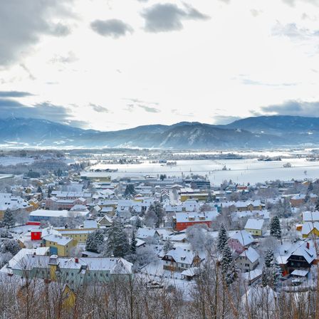 Eine verschneite Stadt mit Häusern und Bergen in der Ferne. Der Himmel ist bewölkt.