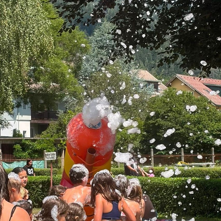 A group of children playing in a bubble machine in a garden with houses in the background.
