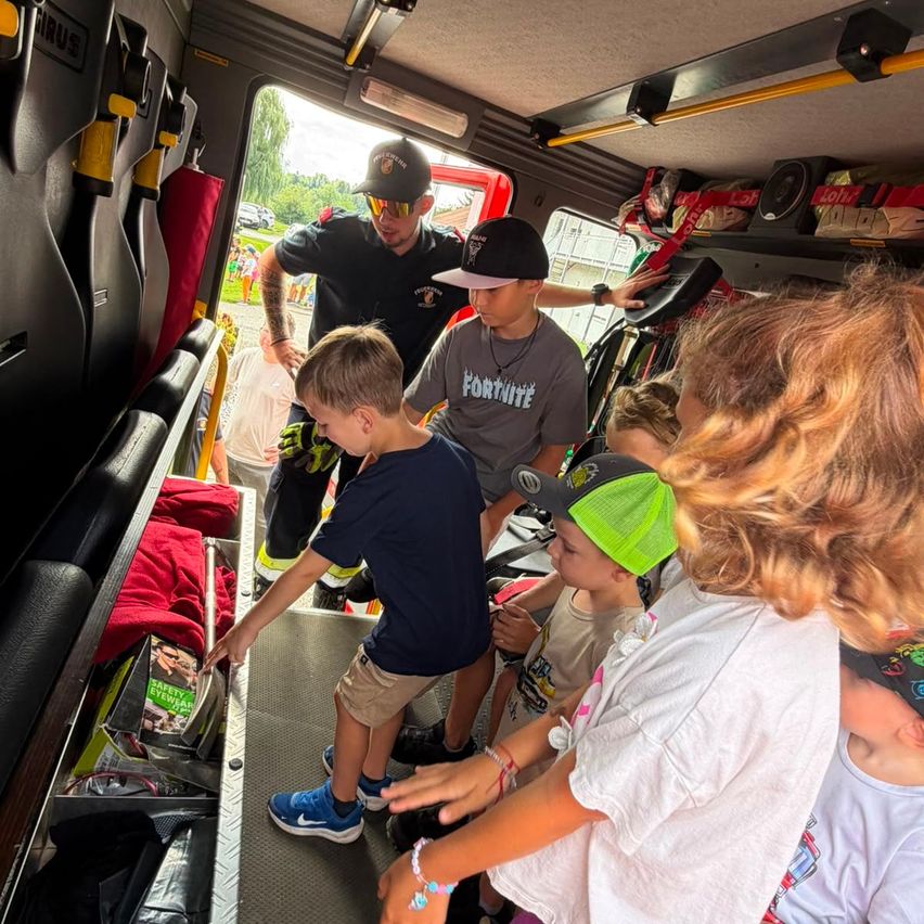 Ein Feuerwehrmann zeigt Kindern das Innere eines Feuerwehrwagens, wobei ein Junge die Ausrüstung untersucht und andere zuschauen.