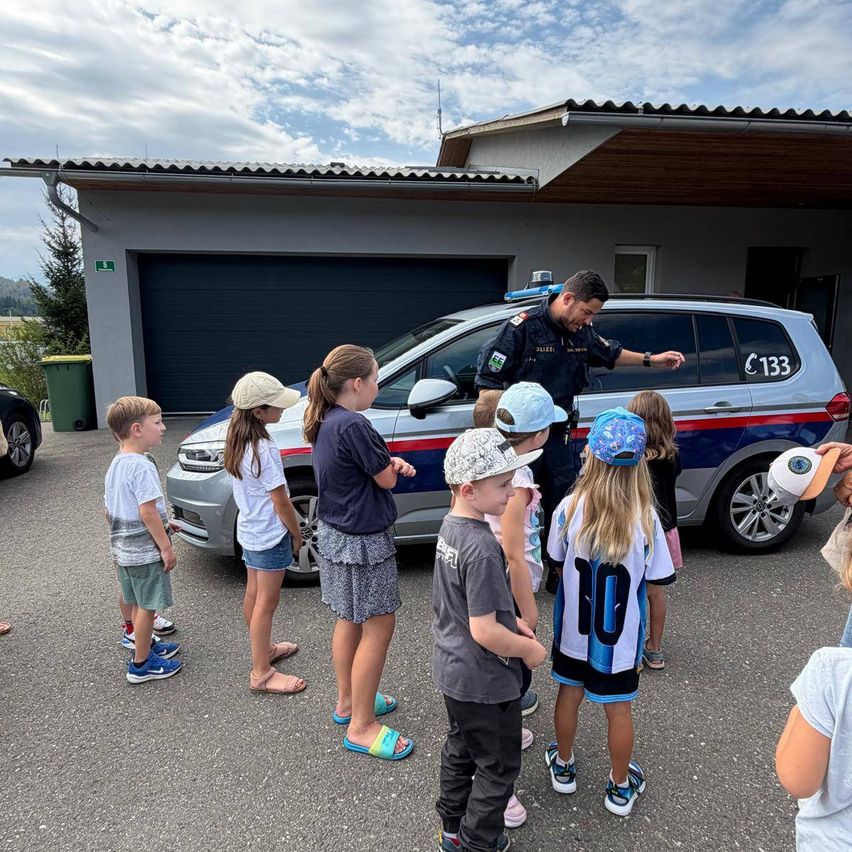 Ein Polizist hält eine Rede vor einer Gruppe von Kindern vor einem Polizeiauto.