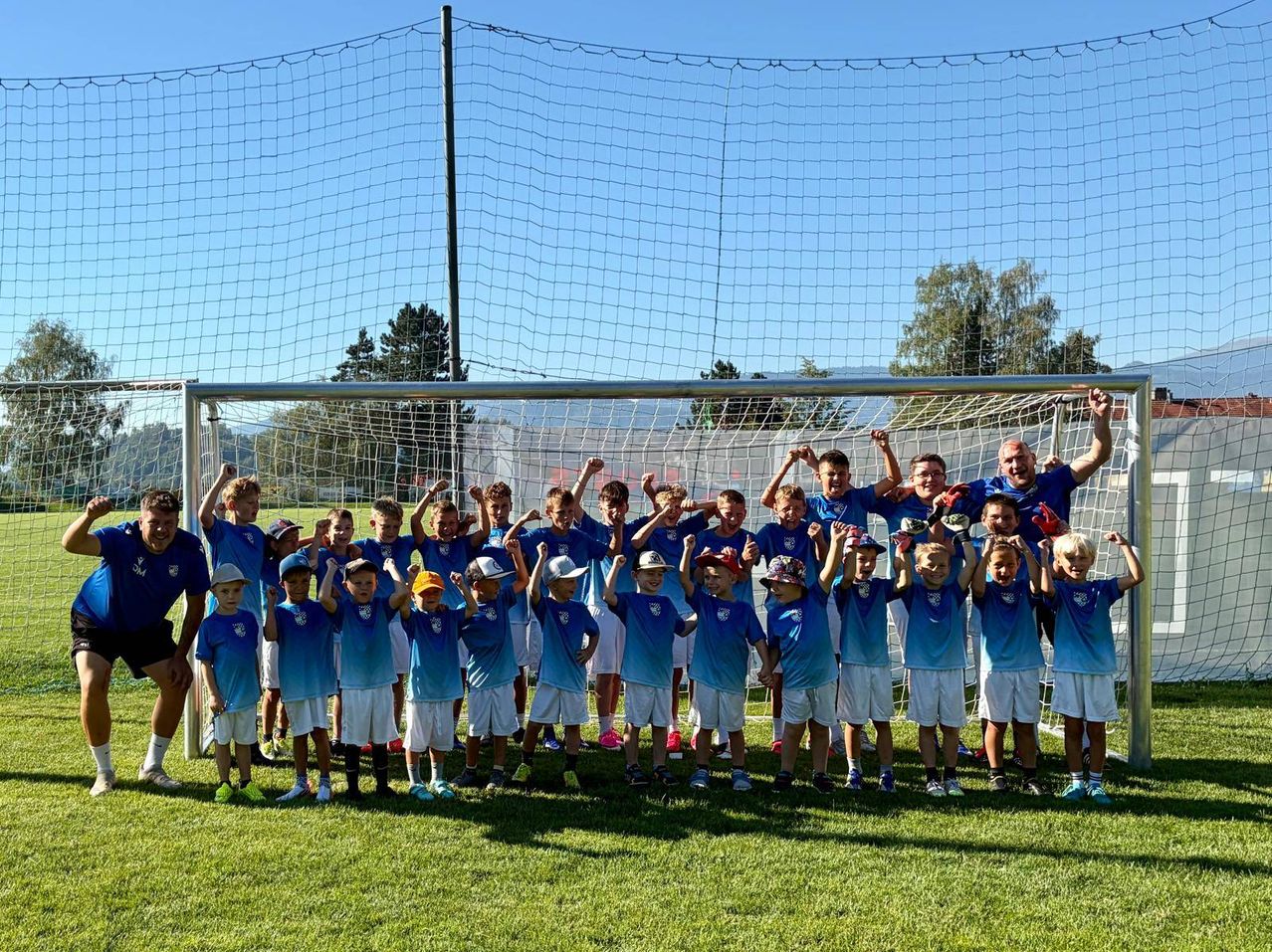 Eine Gruppe junger Jungen in blauen Trikots und weißen Shorts posiert für ein Foto vor einem Fußballtor.