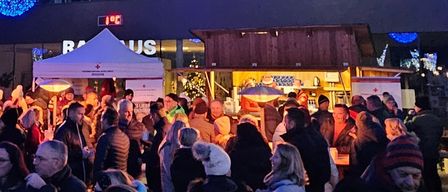 Eine große Menschenmenge versammelt sich drinnen unter einer festlichen blauen Lichtshow, mit Zelten und Ständen rundherum. Die Leute sind warm in Winterkleidung gekleidet.