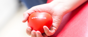 Eine Person hält einen roten Ball mit der Website www.beat.at darauf. Die Hand ist verschwommen und der Hintergrund leicht unscharf.