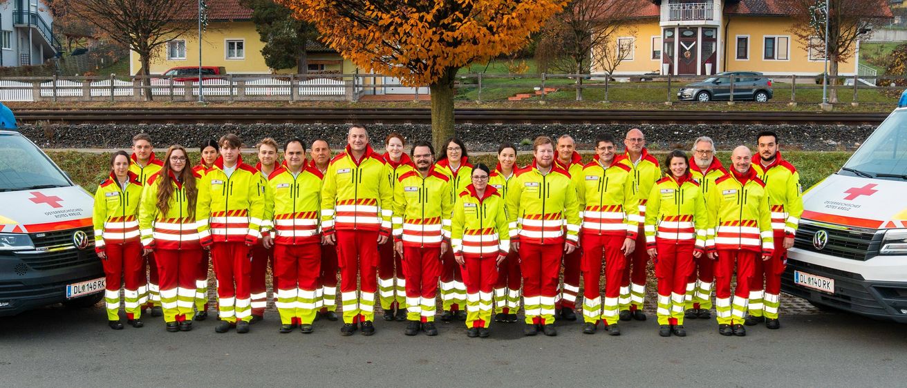 Eine Gruppe von Menschen in leuchtenden gelben und roten Sicherheitsanzügen posiert für ein Foto in der Nähe eines Baumes und einer Eisenbahnstrecke.