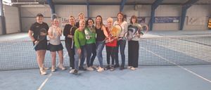 Eine Gruppe von Frauen posiert für ein Foto auf einem Tennisplatz. Sie halten Tennisschläger in den Händen und tragen Turnschuhe.