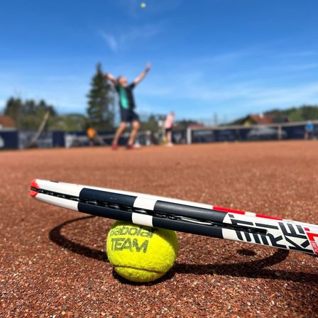 Ein Tennisspieler schlägt einen Tennisball in die Luft, während ein Tennisschläger auf dem Platz liegt.