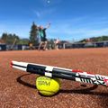 Ein Tennisspieler schlägt einen Tennisball in die Luft, während ein Tennisschläger auf dem Platz liegt.