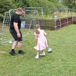 Ein Mann und ein Mädchen spielen Fußball im Garten. Der Mann steht in der Nähe des Tores und das Mädchen kickt den Ball.