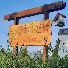 Ein Holzschild mit der Aufschrift 'Kindergarten' steht in einem grünen Busch, mit einem Vogelhaus an der Spitze des Schildes und einem Straßenlicht im Hintergrund.