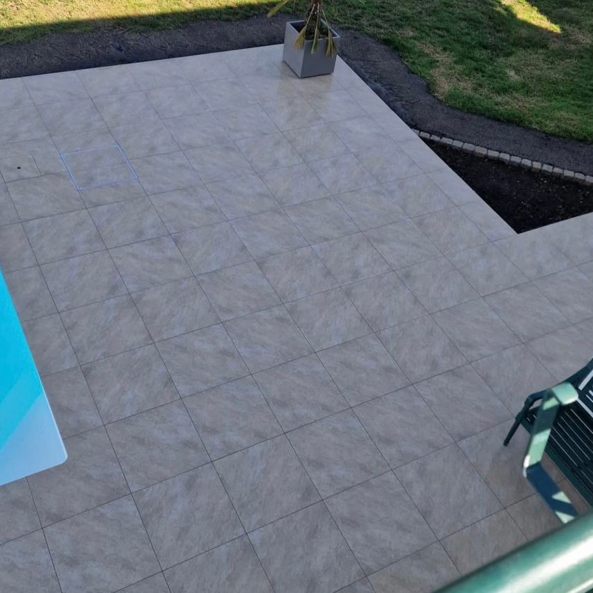Eine Draufsicht auf eine geflieste Terrasse mit einem Topf und einem grünen Stuhl an der Seite. Der Boden ist sauber und gepflegt.