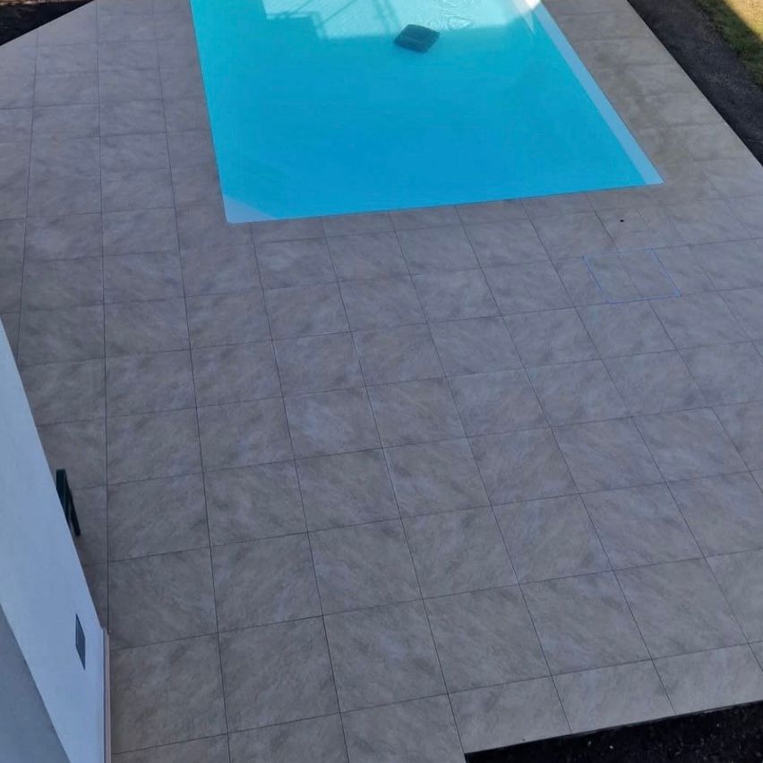 Eine Vogelperspektive eines rechteckigen Schwimmbeckens mit klarem blauem Wasser. Das Becken ist von gefliesten Böden umgeben und hat ein kleines schwarzes Objekt, das in der Mitte schwimmt.