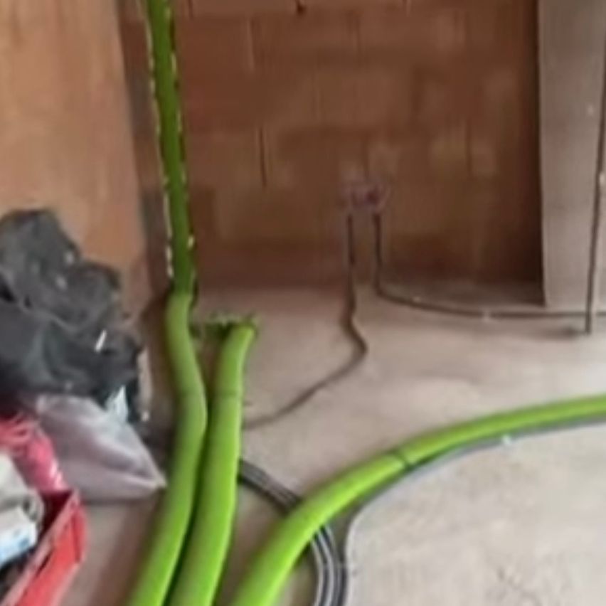 A construction site with green pipes on the floor, a brown wall, and scattered materials. An open door leads to another room.