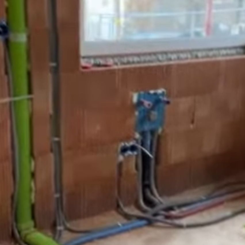 An interior view of a building with electrical wiring. The walls are brown, and there is a window with a reflection of another building.