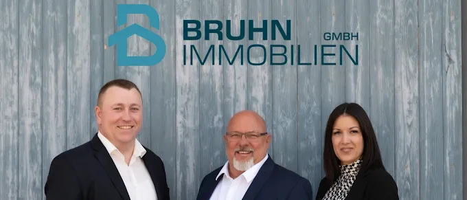Drei Personen stehen vor einer Holzwand mit dem Firmenlogo Bruhn Immobilien.