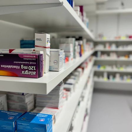 Ein Apothekenregal mit verschiedenen Medikamenten, einschließlich einer Box Antihistaminika und anderen verschreibungspflichtigen Medikamenten.