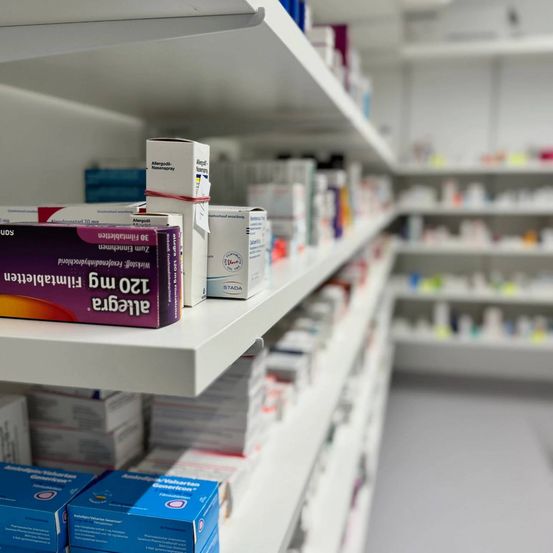 Ein Apothekenregal mit verschiedenen Medikamenten, einschließlich einer Box Antihistaminika und anderen verschreibungspflichtigen Medikamenten.