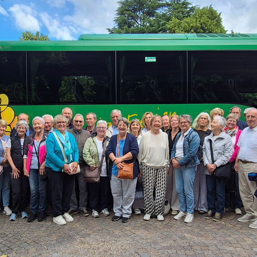 A group of elderly people stands in front of a green bus with a smiling face on the side, likely posing for a photo.