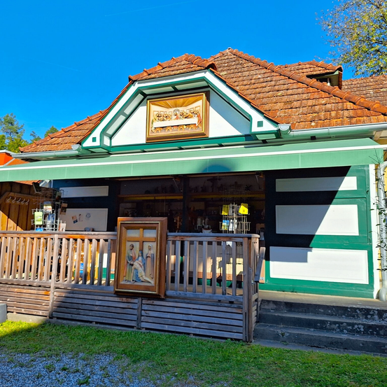 Ein kleines grün-weißes Gebäude mit einem braunen Dach, einem grünen Vordach und einem Holzzaun. Über dem Eingang hängt ein gerahmtes Bild von Jesus und seinen Jüngern.